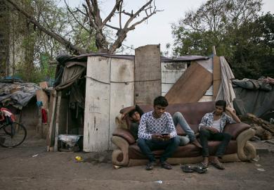 India young men sit on a sofa in a slum, illustrating graduate unemployment