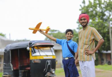 A young Indian rikshaw driver and his little brother holding a toy plane, symbolising international education