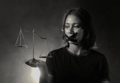 A woman wide tape over her mouth holds uneven scales of justice