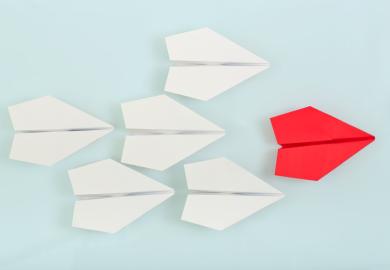 Red paper plane leading white paper planes