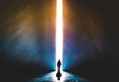 A man stands in front of a shaft of light in a dark room