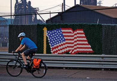 Man riding bicycle past United States of America flag