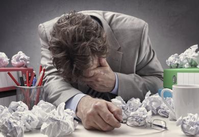 Man with head in hand surrounded by paper