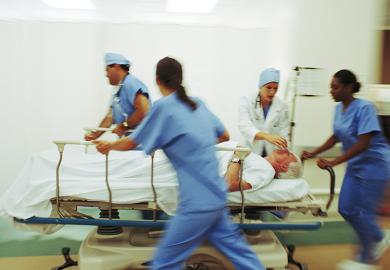 Four medics pushing mature male patient through hospital corridor on trolley.
