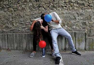 Two young people inhale nitrous oxide from balloons
