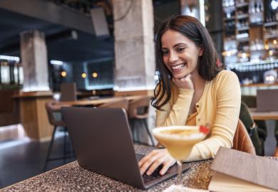 A woman drinks a cocktail and works on her laptop, symbolising residential courses