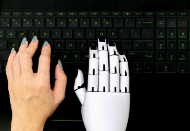 A robot and human hand on a computer keyboard, symbolising AI-assisted writing