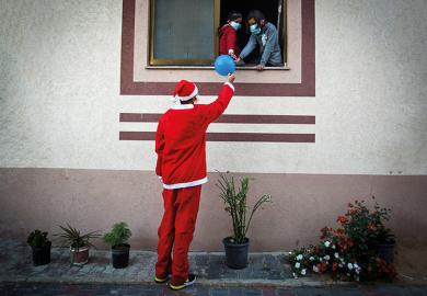 Man dressed as Santa passes a balloon to people through a window