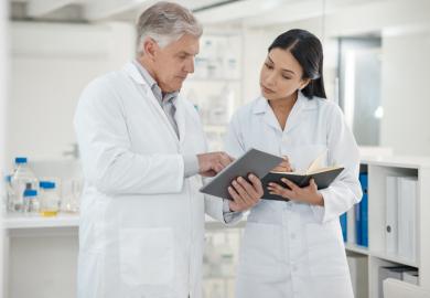A senior scientist shows a junior scientist something on a tablet