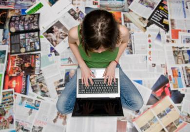 A woman types on her laptop on a carpet of newspapers, symbolising student journalism