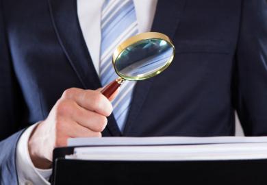 Suited businessman examining paperwork with magnifying glass