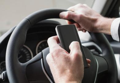 Suited man typing on phone while driving