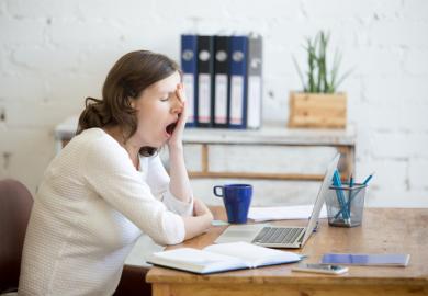 A woman yawns at a desk