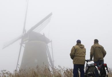 Two cyclists standing in fog looking at windmill
