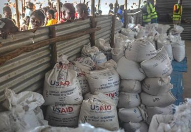 Congolese refugees look through a corrugated metal fence at the final batches of food delivered by the now-dismantled USAID in May 2025