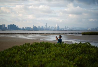 A man takes a photo from the shoreline of Hong Kong’s Deep Bay with the skyline of Chinese mainland city of Shenzhen visible behind him
