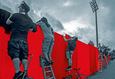 Men trying to look or climb over a wall