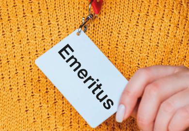 Close up of a hand holding badge name tag reading 'Emeritus' to illustrate Why I am not going to call myself a ‘professor emerita’