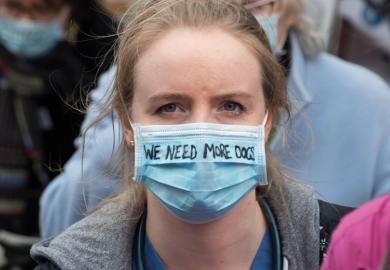 A woman doctor wears a surgical mask with the writing 'We need More Docs' to illustrate More medical students ‘won’t solve doctor shortage alone’