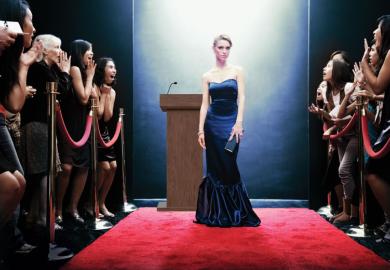 celebrity on red carpet, crowd behind barriers looking excited at seeing her.