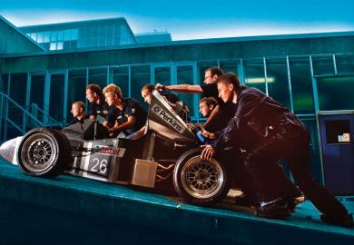 Students push a racing car up a ramp at Bath University to illustrate fostering belonging will attract students to campus