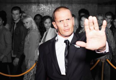 Bouncer with arm outstretched outside nightclub