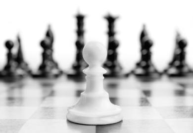 White chess pawn in foreground ahead of black pieces