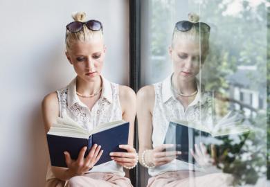 A woman reads a book on a window bench, with a reflection of her doing so in the window, illustrating duplicate publication reading a book