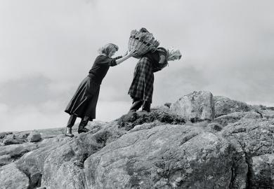 Women carrying basket up rocks
