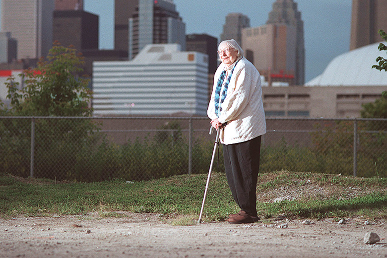 Jane Jacobs walking with city skyline in background