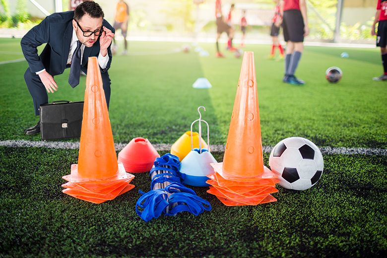 Man in a suit looking at soccer practice equipment rather than the players on the pitch. To illustrate that it is difficult to see Skills England having any influence on policy.