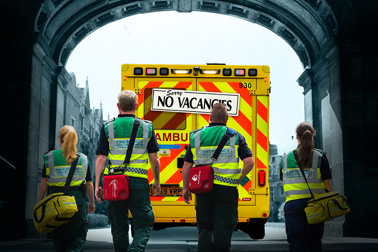 Paramedics leaving a university walking towards an ambulance with a ‘no vacancies’ sign, to illustrate the lack of positions for medical graduates.