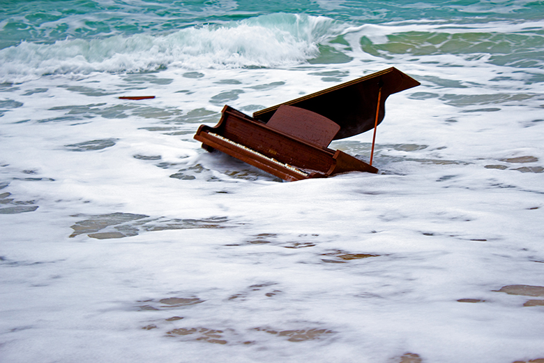 Piano breaking in the sea, illustrating threats to the creative industries in the UK without adequate university funding.