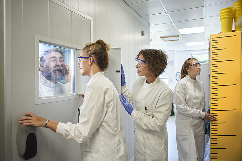 A senior academic trying to shout through a glass window at young researchers in a laboratory using metrics. To illustrate that messaging around the use of metrics is not always heard. A senior academic trying to shout through a glass window at young researchers in a laboratory using metrics. To illustrate that messaging around the use of metrics is not always heard.