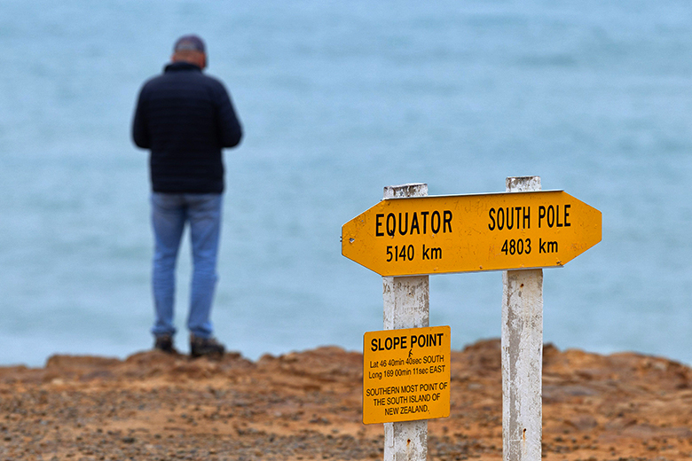 Visitor at Slope Point signpost showing distances to the Equator and South Pole, Southland, South Island, New Zealand.