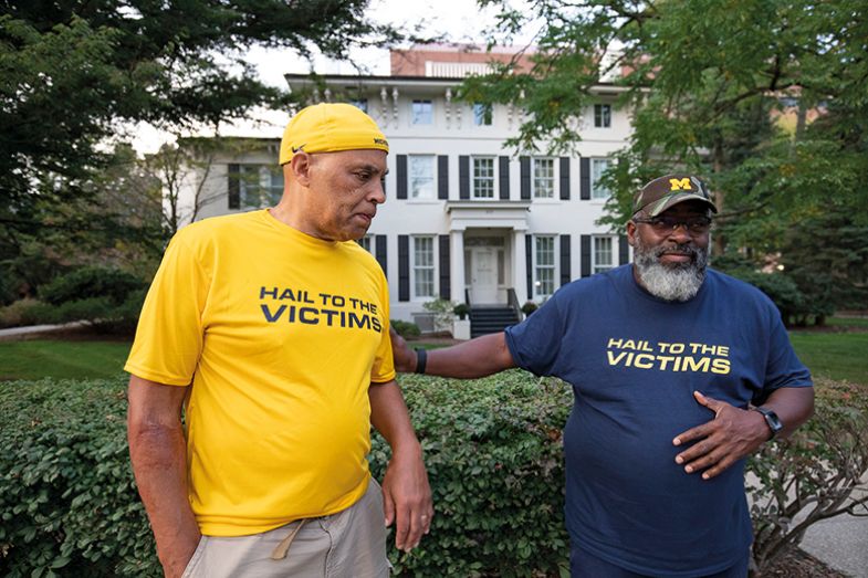 Chuck Christian (L) and former University of Michigan football player Jonathon Vaughn, who says he was sexually assaulted by former UM sports doctor Robert Anderson, take part in a vigil outside the home of outgoing University of Michigan President Mark S