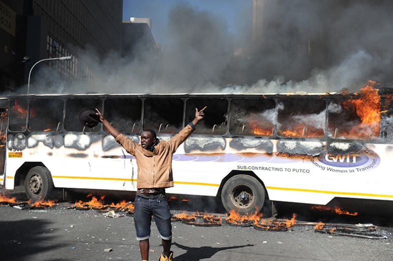 A Wits University student throws stones while a bus burns during the #FeesMustFall protests on 10 October 2016 in Johannesburg, South Africa. A Wits University student throws stones while a bus burns during the #FeesMustFall protests on 10 October 2016 in Johannesburg, South Africa.