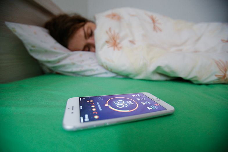 A woman sleeps, with a health app on her phone in the foreground