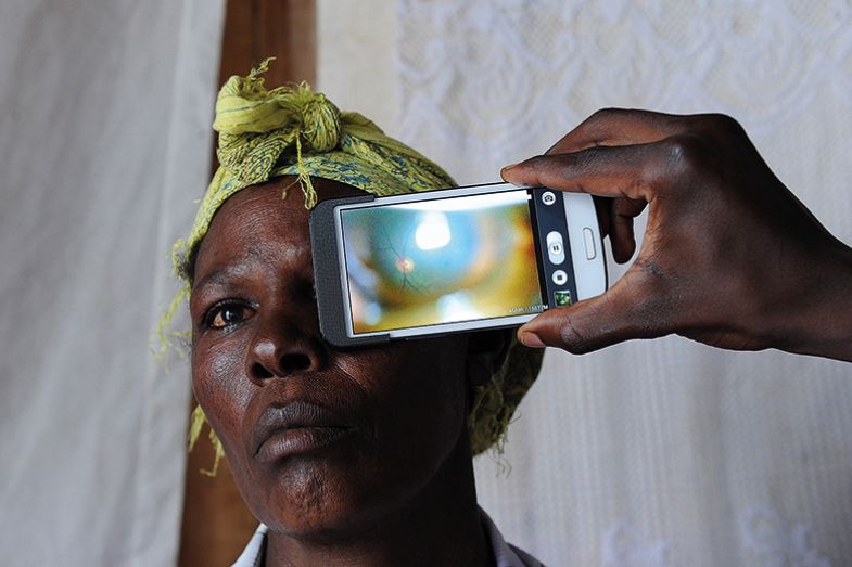 A technician in Kenya scans the eye of a woman with a phone app (used to scan people's eyes and optic nerves, to detect eye diseases, including cataracts and glaucoma).