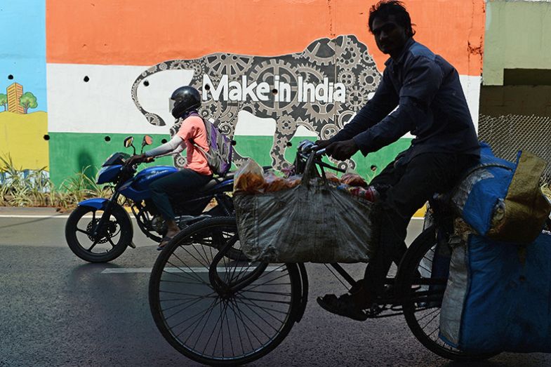 Indian commuters ride past a wall bearing the image of the mascot for ‘Make in India Week’ in Mumbai on 12 February 2016.