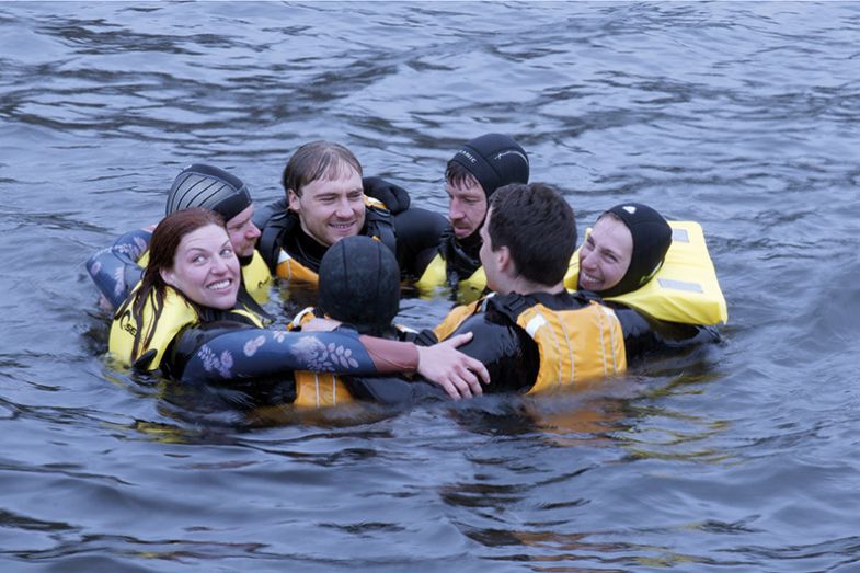 A group of people in wet suits and life preservers in the water