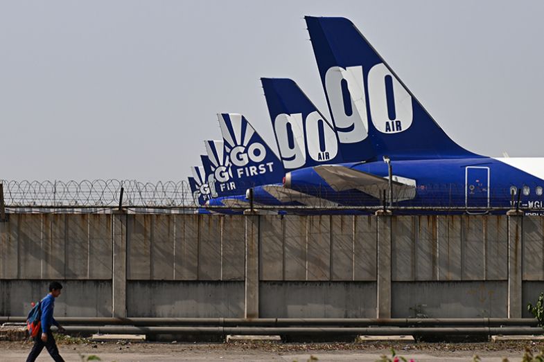 A man walks on a road past Go First aircrafts, that are parked at the tarmac at the airport in New Delhi, India, 2023. To illustrate Asian students deciding on where to study. A man walks on a road past Go First aircrafts, that are parked at the tarmac at the airport in New Delhi, India, 2023. To illustrate Asian students deciding on where to study.