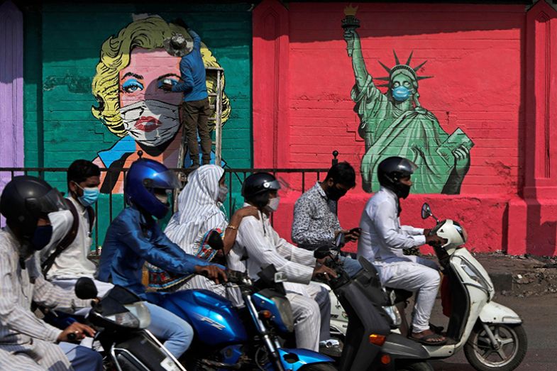 People on mopeds drive past an artist painting a mural of Marilyn Monroe, beside one of the Statue of Liberty wearing face masks in Mumbai, India, 2021. To illustrate Asian students being put off studying in the US, especially after Covid. People on mopeds drive past an artist painting a mural of Marilyn Monroe, beside one of the Statue of Liberty wearing face masks in Mumbai, India, 2021. To illustrate Asian students being put off studying in the US, especially after Covid.