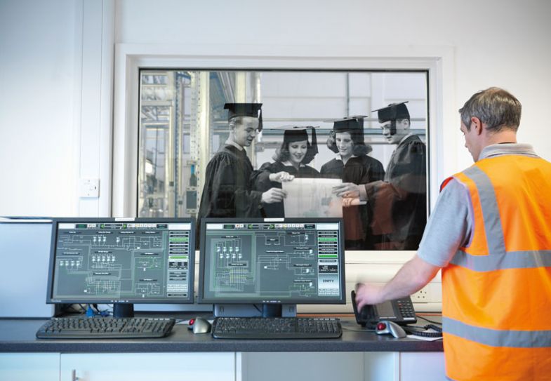 Worker with computers with graduates behind glass looking at paper