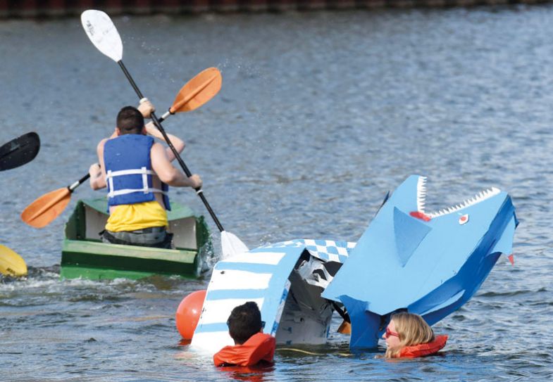 Teams compete during the Rock the Boat cardboard boat race with a lady in the water to illustrate Sinking or swimming