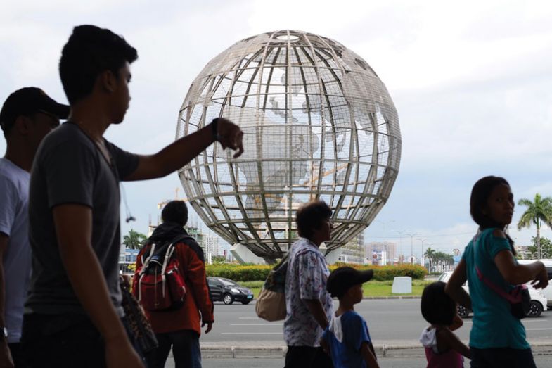 People pass by a steel globe sculpture at a mall in Manila, Philippines.