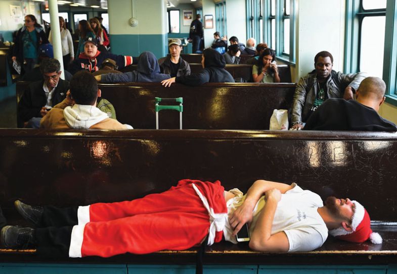 A man dressed in a Santa outfit sleeps on the Staten Island during the SantaCon in New York City to illustrate exhaustion
