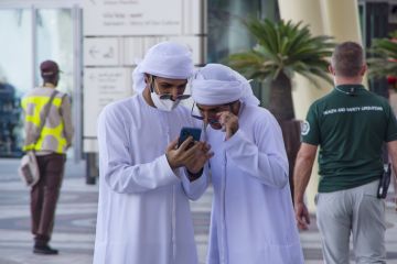 13 November 2021 UAE, Dubai. Arab men dressed in white Disdasha or Kandura smiling while reading a message on the phone.