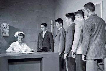A nurse sitting at a table with a queue of people waiting to speak to her A nurse sitting at a table with a queue of people waiting to speak to her