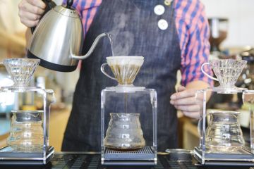 A barista's hands are seen pouring boiling water to make filter coffee.